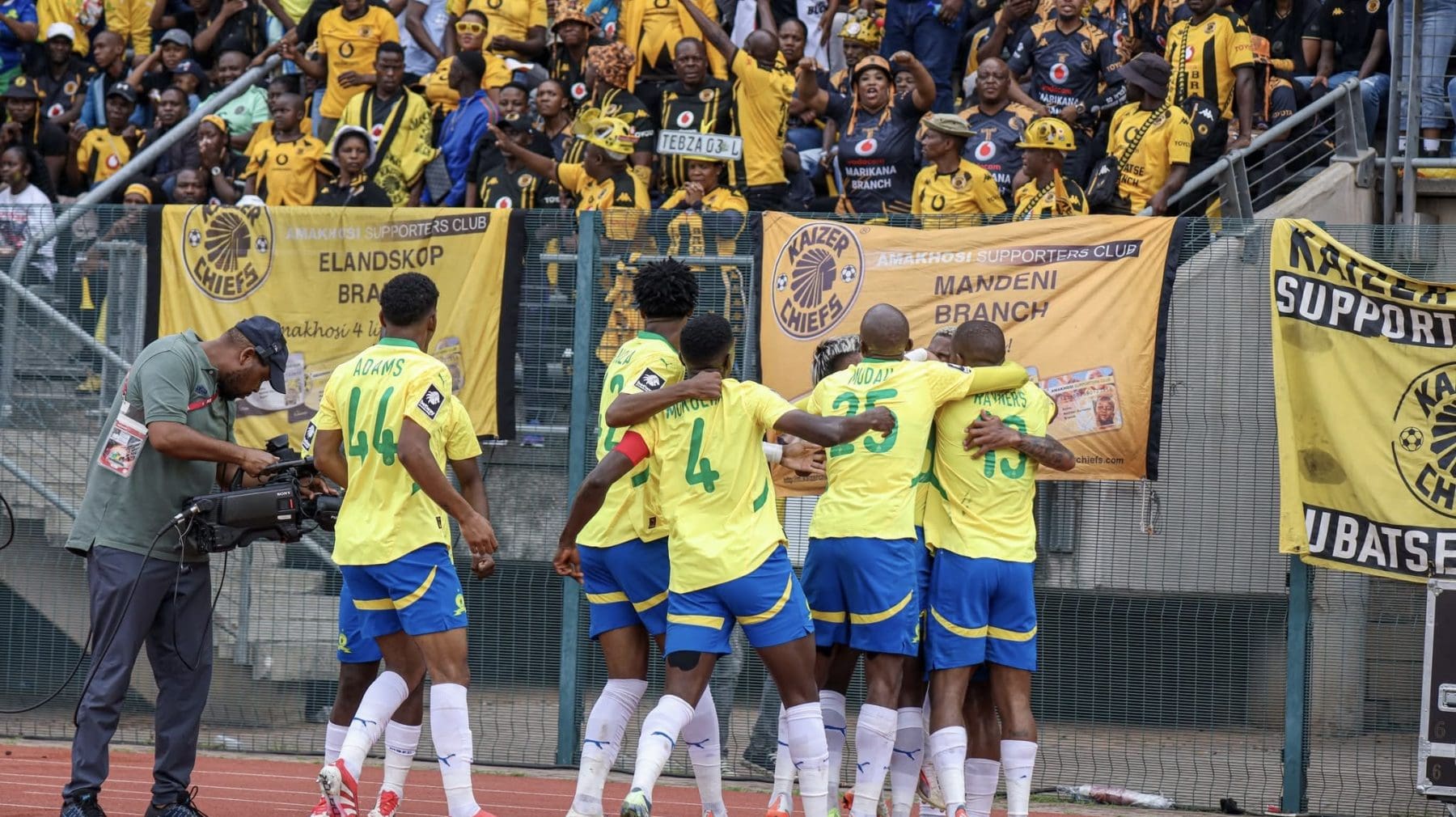 Mamelodi Sundowns players celebrating a goal in front of Kaizer Chiefs fans 